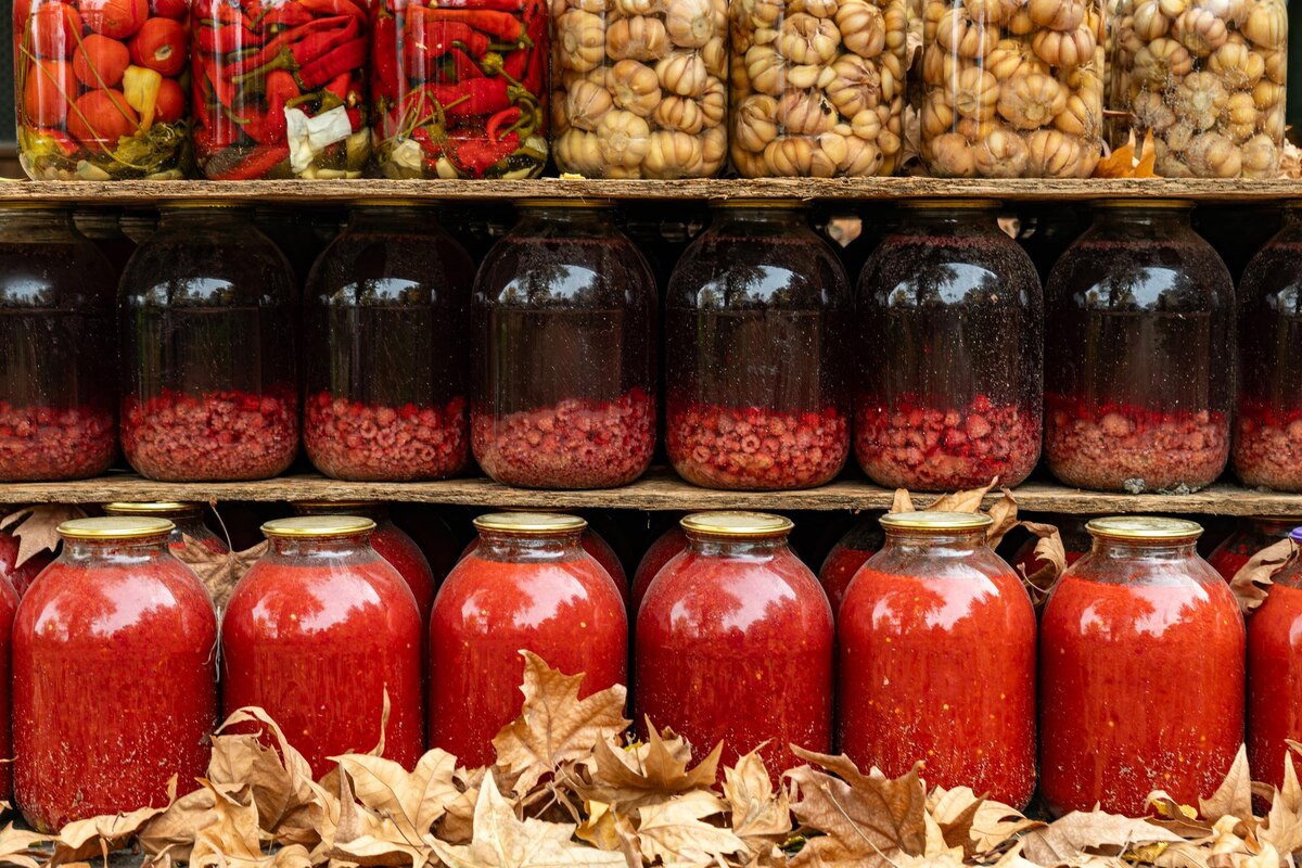 Glass mason jars filled with home-preserved vegetables and jam on a wooden shelf
